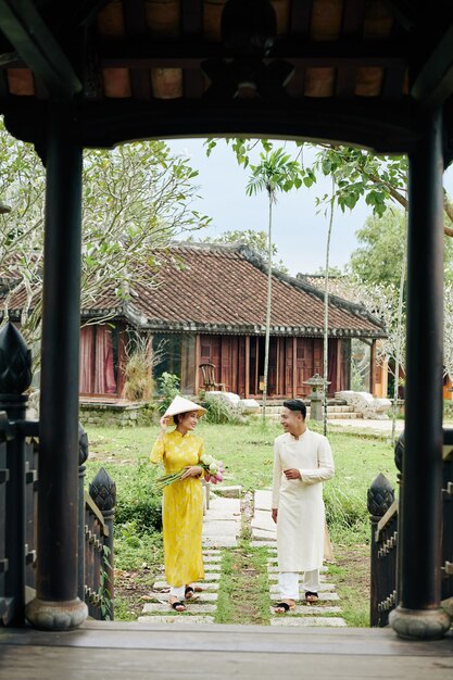 Feliz pareja asiática joven en vestidos de ao dai caminando al templo