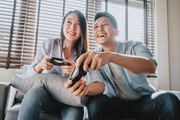 Feliz pareja asiática jugando videojuegos juntos en su sala de estar y divirtiéndose
