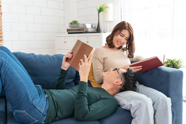 Feliz pareja asiática pasa el fin de semana juntos en el sofá en casa relajándose y disfrutando de la lectura del libro