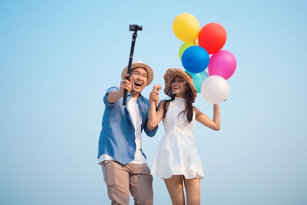 Feliz pareja asiática selfie fotos junto con globos de colores junto al mar