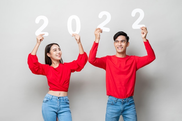 Feliz pareja asiática sonriendo y levantando la mano mostrando el número 2022 para el concepto de año nuevo en el fondo gris claro del estudio