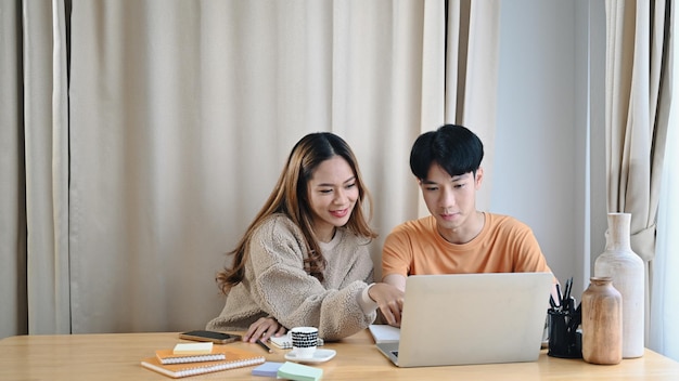 Feliz pareja asiática usando computadora portátil en casa