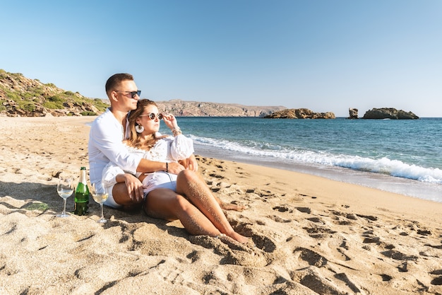 Feliz pareja de asientos con champán en la playa