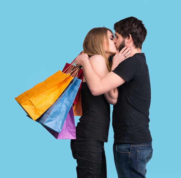 Feliz pareja besándose con bolsas de la compra sobre un fondo azul.