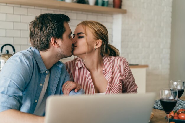 Feliz pareja besándose mientras usa la computadora portátil