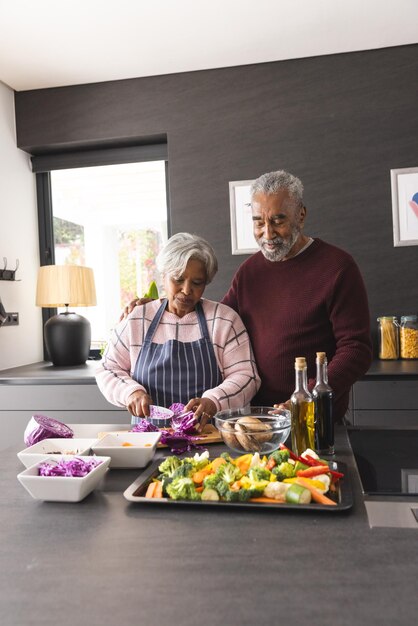 Una feliz pareja biracial senior preparando verduras y abrazándose en la cocina en casa, espacio de copia