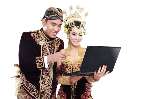 Feliz pareja de boda tradicional java con laptop