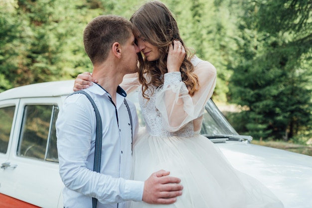 Feliz pareja de bodas de lujo besándose y abrazándose cerca de un auto retro.