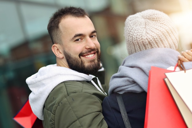 Feliz pareja con bolsas de la compra después de ir de compras en la ciudad sonriendo y abrazándose