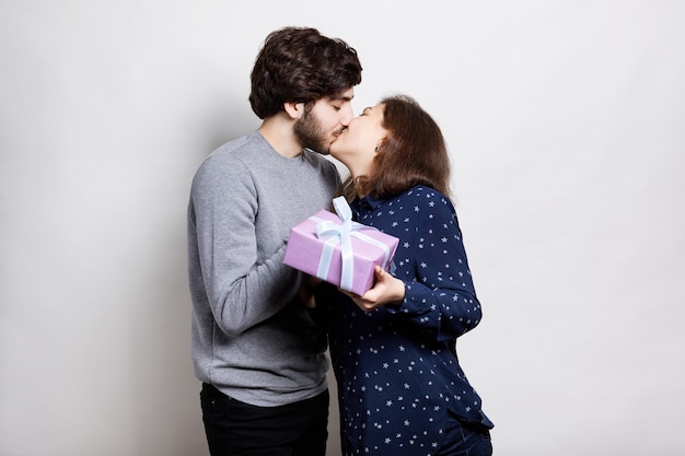 Feliz pareja con caja de regalo rosa besándose apasionadamente