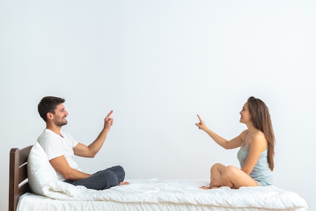 La feliz pareja en la cama gesticulando sobre el fondo blanco.