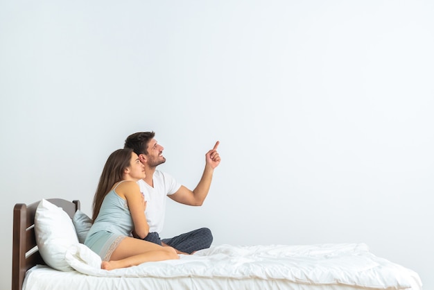 La feliz pareja en la cama gesticulando sobre el fondo blanco.