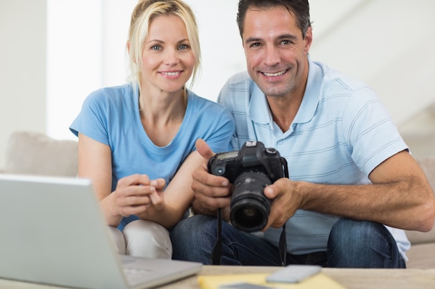 Feliz pareja con cámara y portátil en el sofá en la sala de estar