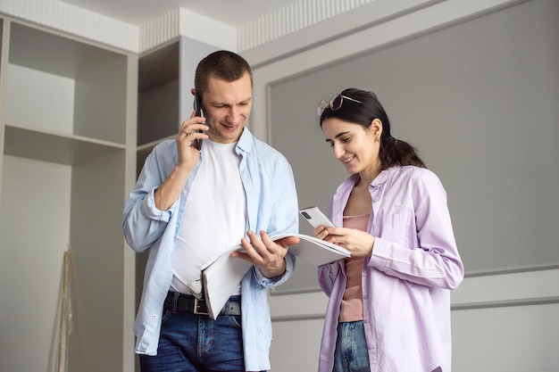 Una feliz pareja casada hablando por teléfono está parada en un apartamento nuevo con un plan de habitación