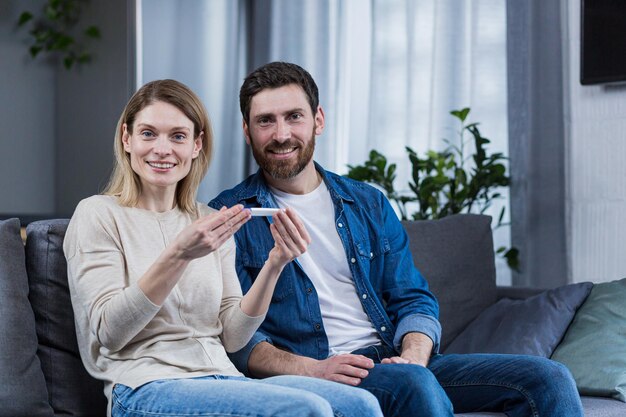 Feliz pareja casada hombre y mujer mirando a la cámara y regocijándose con una prueba de embarazo positiva celebrando la espera de un bebé