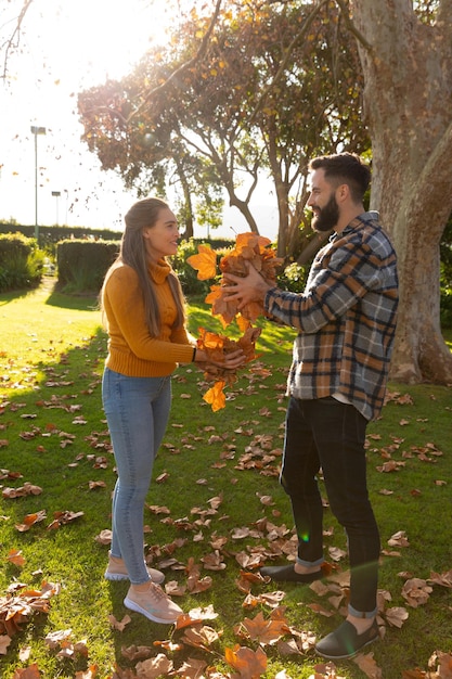 Feliz pareja caucásica divirtiéndose recogiendo hojas en el soleado jardín de otoño. Concepto de vida doméstica, tiempo libre, romance y convivencia.