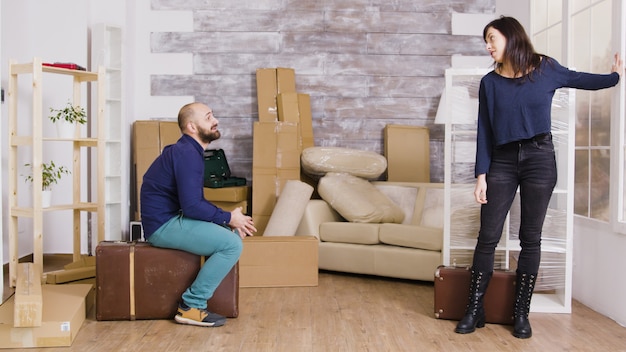 Feliz pareja caucásica llevando maletas en su nuevo apartamento. Cajas de cartón al fondo.