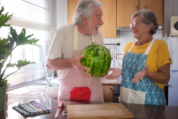 Una feliz pareja caucásica senior en la cocina de su casa sosteniendo una sandía de temporada grande y pesada