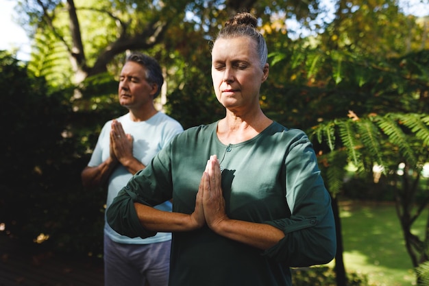 Feliz pareja caucásica senior practicando yoga, meditando en un jardín soleado. jubilación estilo de vida de jubilación saludable, pasar tiempo en casa.