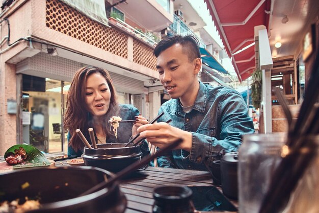 Feliz pareja china joven sentada en el café afuera disfrutando de la comida asiática tradicional. Grabación en pantalla ancha.