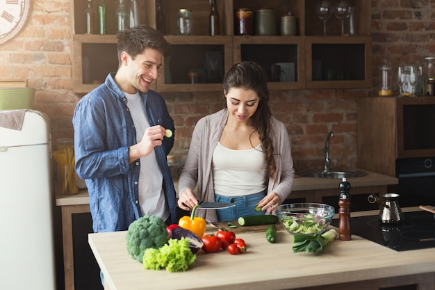 Feliz pareja cocinando alimentos saludables juntos en su cocina tipo loft en casa. Preparando ensalada de verduras.