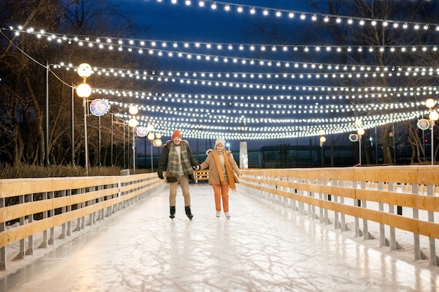 Feliz pareja cogidos de la mano en la pista de patinaje en el parque