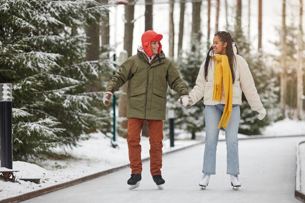 Feliz pareja cogidos de la mano y sonriendo el uno al otro mientras patina en el parque