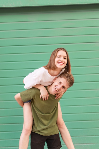 Feliz pareja contra el de una pared de color verde, el niño sostiene a la niña de espaldas