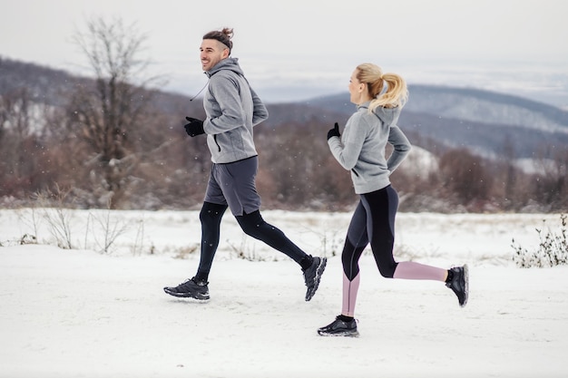 Feliz pareja corriendo juntos en la nieve en la naturaleza en invierno. Estilo de vida saludable, ejercicios cardiovasculares, relación.