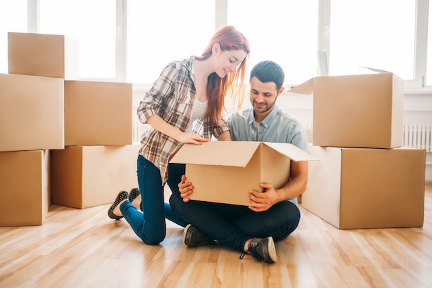 Feliz pareja desembalaje de cajas de cartón con propiedad, inauguración de la casa. Mudarse a una nueva casa