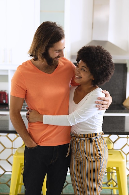 Feliz pareja diversa en la cocina sonriendo y abrazando