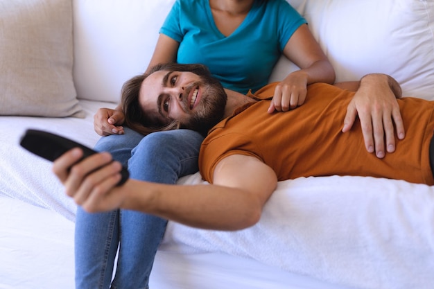 Feliz pareja diversa sentada en el sofá abrazándose y viendo la televisión