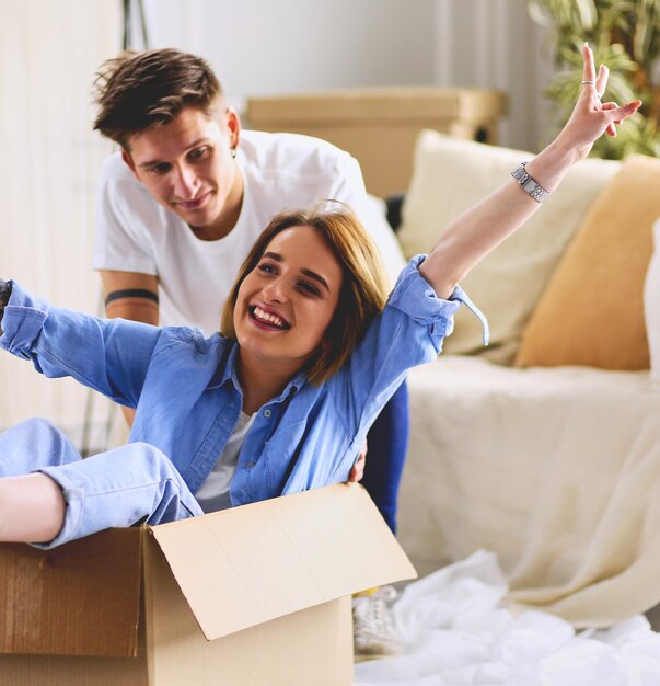 Feliz pareja divirtiéndose y montando en cajas de cartón en casa nueva