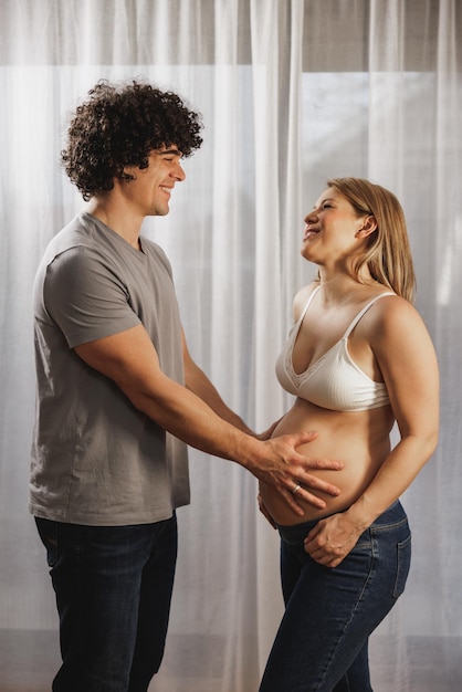 Feliz pareja embarazada enamorada hablando mientras está de pie junto a la ventana en casa.