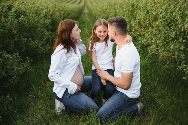 Feliz pareja embarazada con hija en la naturaleza de verano