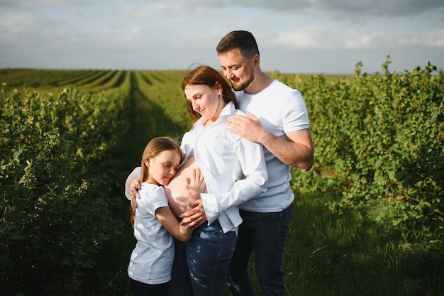 Feliz pareja embarazada con hija en la naturaleza de verano