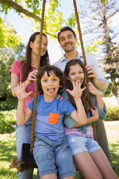 Feliz pareja empujando niños en columpio