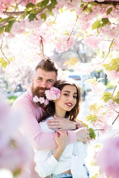 Feliz pareja enamorada entre árboles florecientes Hombre barbudo abraza a mujer sensual Día de San Valentín Su felicidad lo es todo para él Cuidado de la piel y frescura Deseo y romance La primavera es temporada para el amor