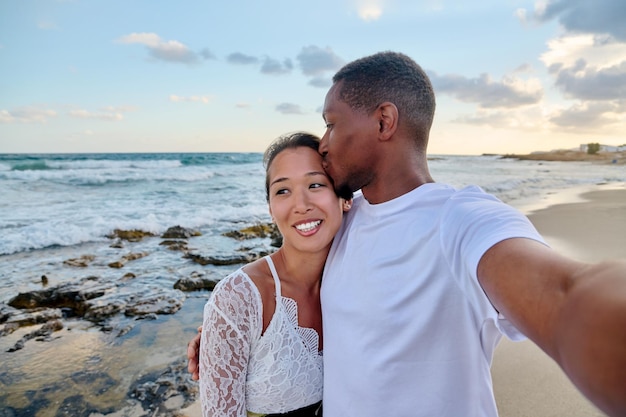 Feliz pareja enamorada besándose tomando selfie juntos en un smartphone en la playa