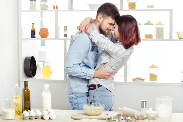 Feliz pareja de enamorados cocinar masa y besarse en la cocina