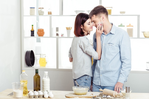 Feliz pareja de enamorados cocinar masa y besarse en la cocina