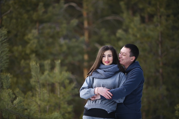 Feliz pareja de enamorados cubiertos con una manta en el fondo de un bosque nevado de invierno