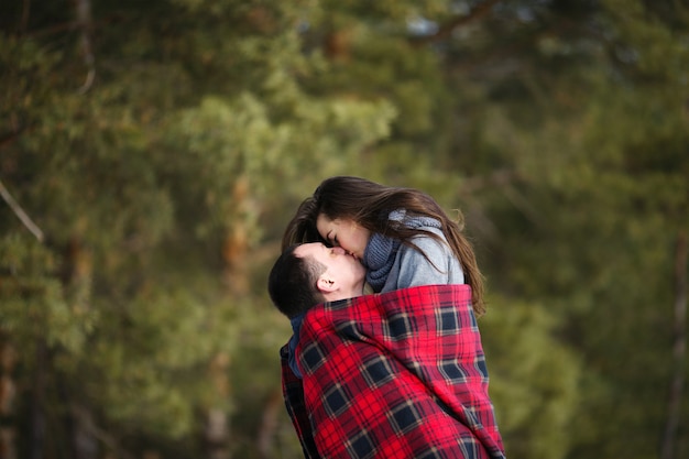 Feliz pareja de enamorados cubiertos con una manta en el fondo de un bosque nevado de invierno