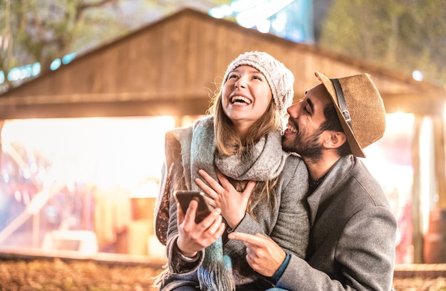 Feliz pareja de enamorados divirtiéndose con teléfonos móviles inteligentes en invierno