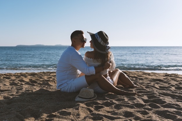 Feliz pareja de enamorados está sentado en la playa durante el atardecer o el amanecer