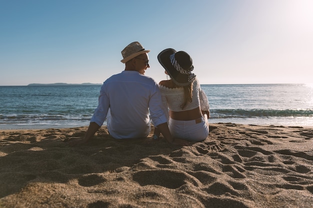 Feliz pareja de enamorados está sentado en la playa durante el atardecer o el amanecer