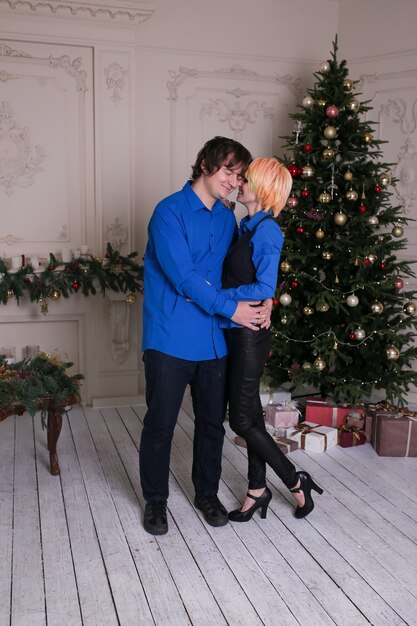 Feliz pareja de enamorados de pie en casa en el árbol de Navidad en el fondo