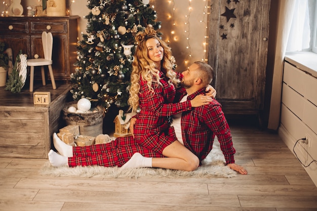 Feliz pareja de enamorados sentados junto al árbol de Navidad en el suelo de una casa. Concepto de vacaciones