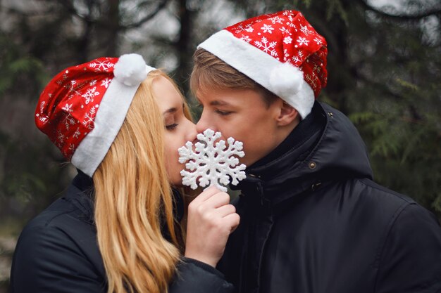 Feliz pareja de enamorados con sombreros de Santa besándose y sosteniendo un gran copo de nieve