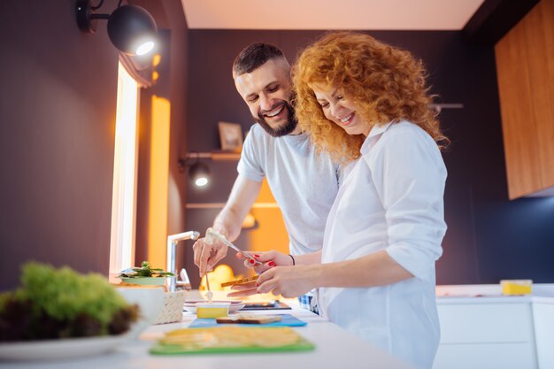 Feliz pareja encantada preparando sándwiches en la cocina